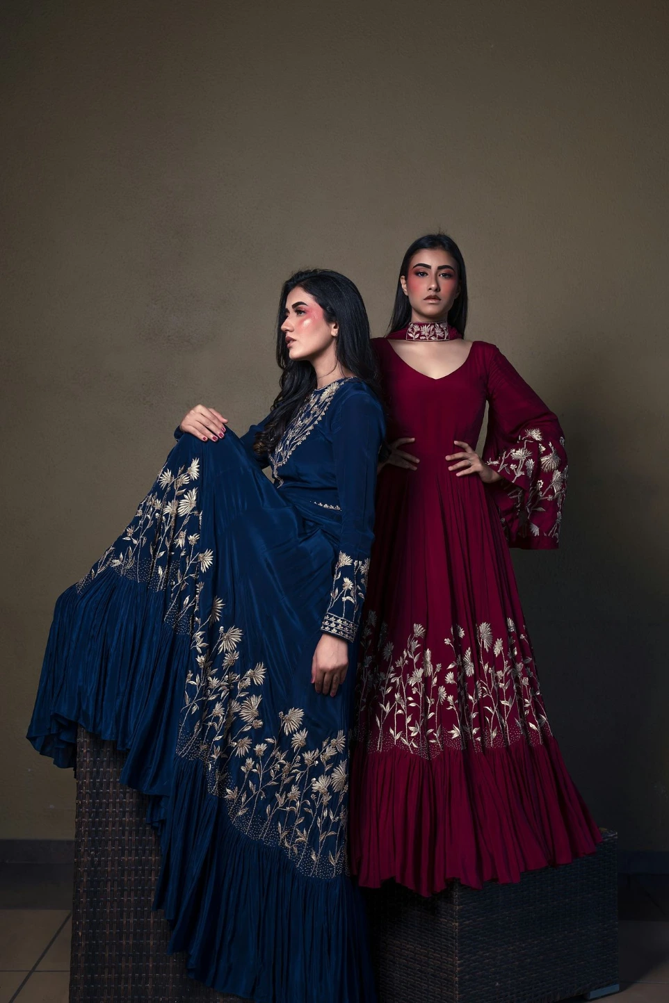 Two women in ornate gowns posing against a muted background.